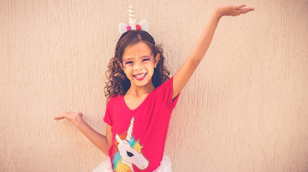 happy girl wearing unicorn headband, unicorn shirt, and tutu | 19 Easy Homemade Halloween Costumes You Can Make For Your Kids | Featured